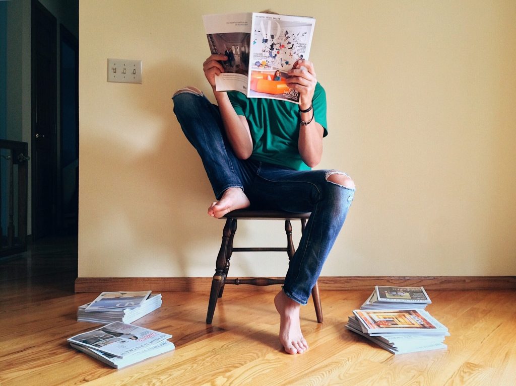 Personne sur une chaise qui lit un magazine, il y a d'autres piles de magazine à ses pieds